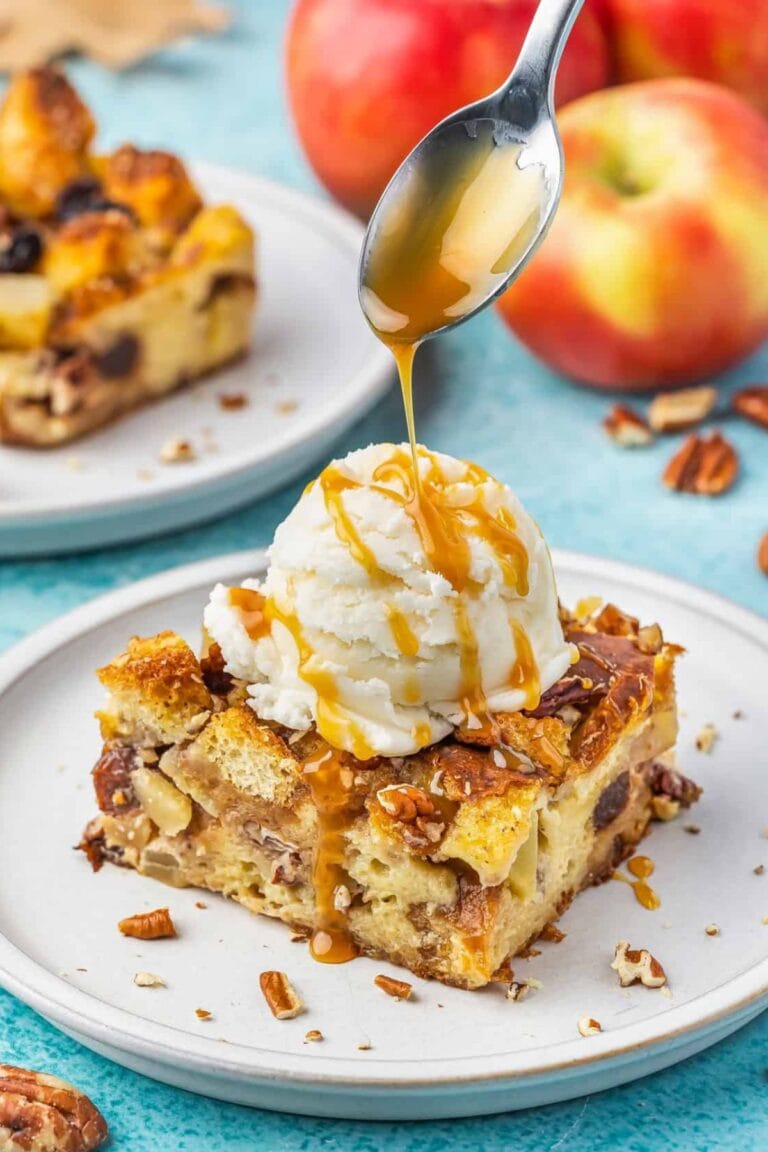 Slice of apple bread pudding with scoop of vanilla ice cream on top and caramel sauce being drizzled over the top.