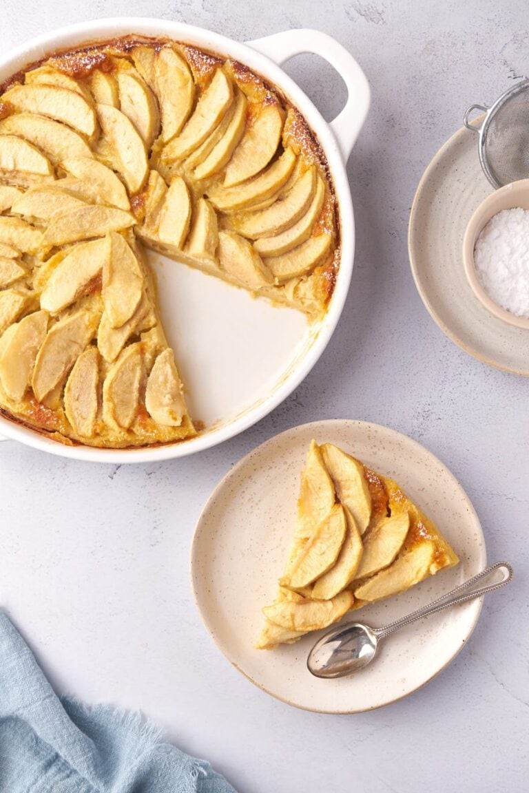 Apple clafoutis with a slice removed and sitting on a dessert plate.