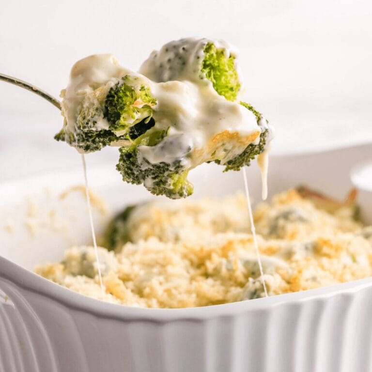 Spoonful of broccoli au gratin being lifted up from white casserole dish.