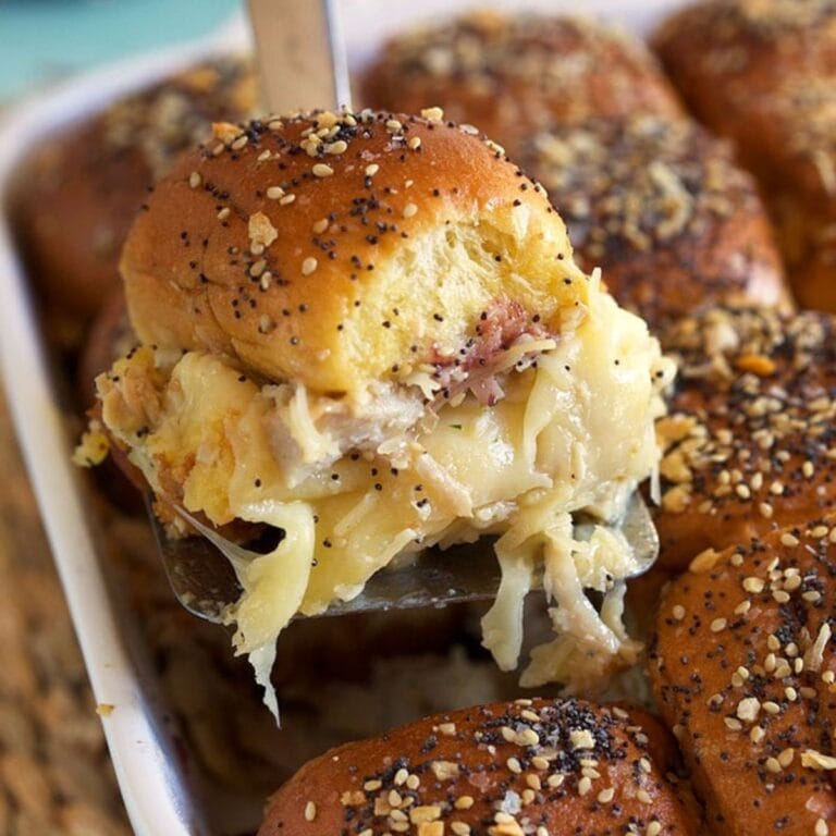 Spatula lifting out a cheesy turkey slider from baking dish.