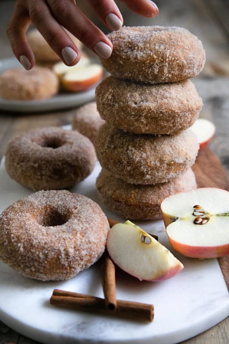 Hand stacking cinnamon sugar baked apple donuts on a plate.