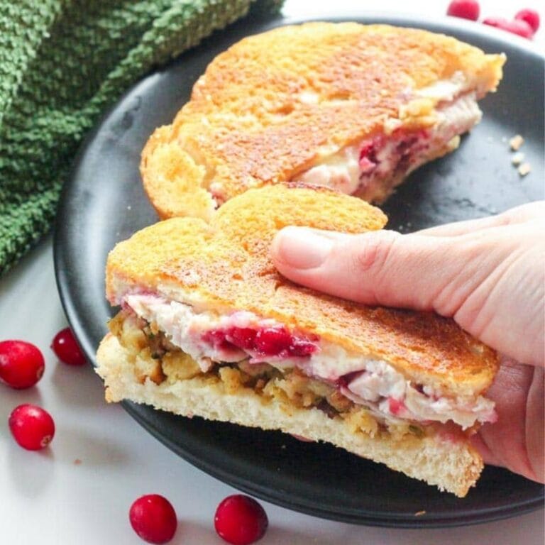 Hand picking up half of a grilled turkey cranberry cream cheese sandwich from a black plate.