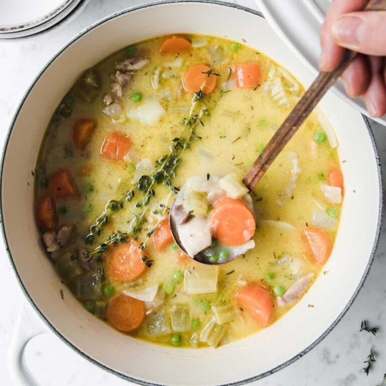 Turkey stew being stirred in a white Dutch oven.