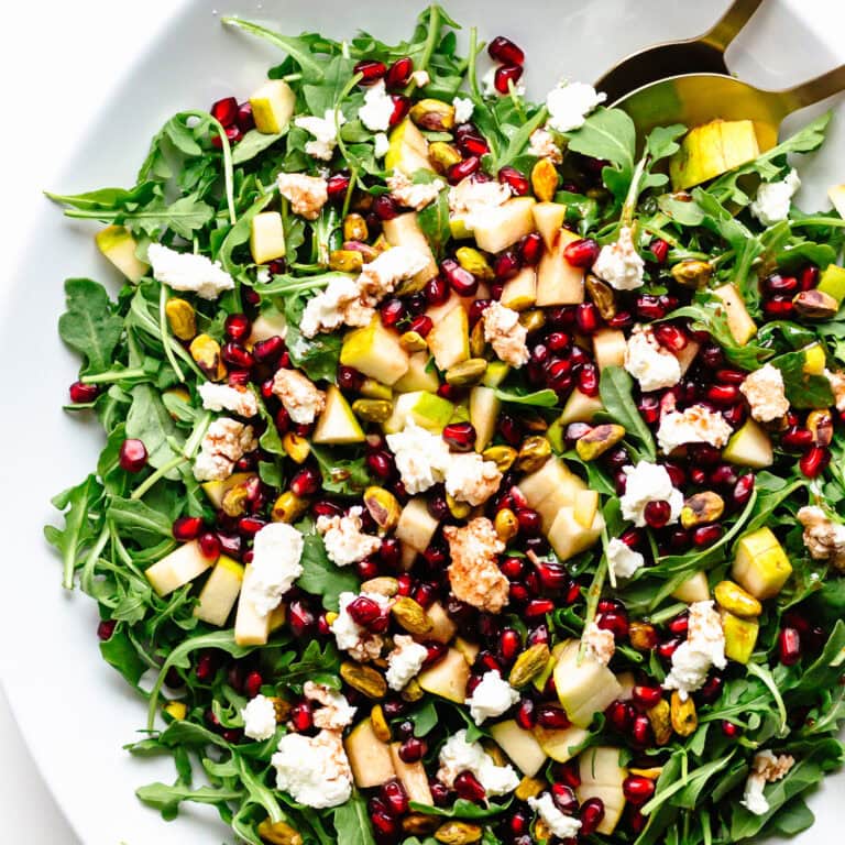 Holiday salad on a white platter with baby greens, pear, pomegranate, pistachios, goat cheese and pomegranate vinaigrette. 