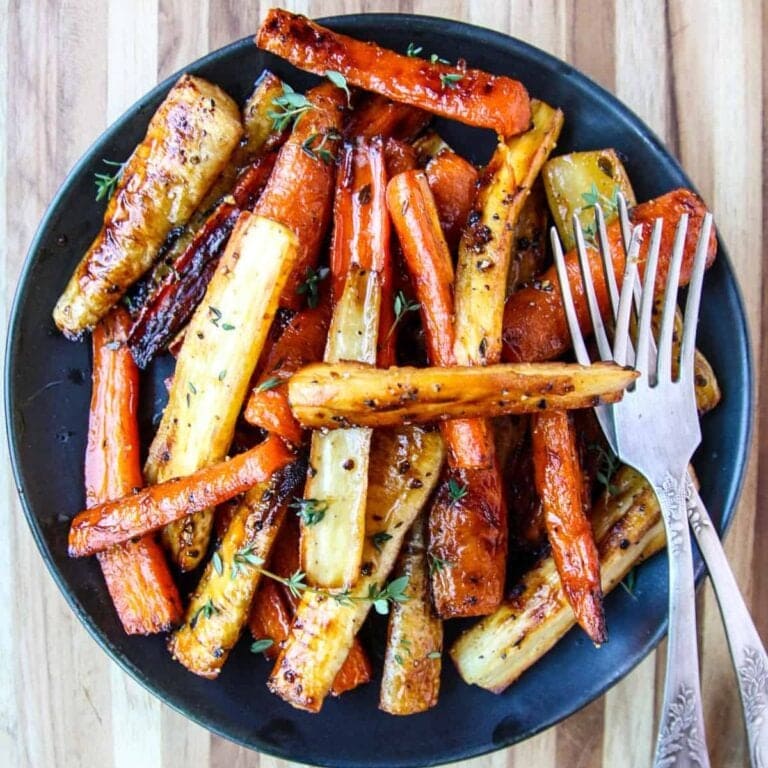 Honey roasted carrots and parsnips on a black plate with serving forks.