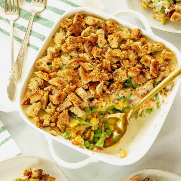 Mixed vegetable casserole in white baking dish with serving spoon scooping some out.
