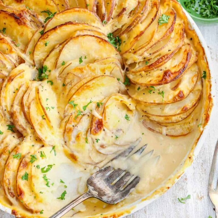 Potatoes au gratin in white circular baking dish with serving fork.
