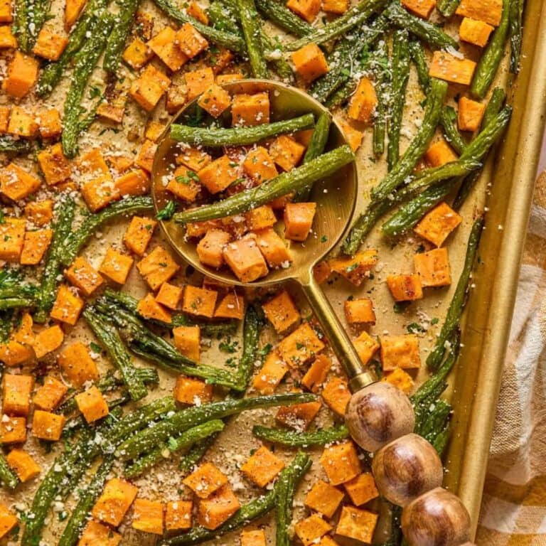 Roasted sweet potatoes and green beans on a baking sheet with large serving spoon.