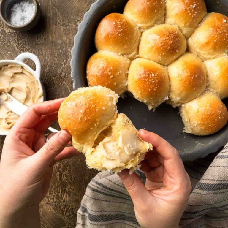 Hand holding a soft dinner roll spread with maple butter.