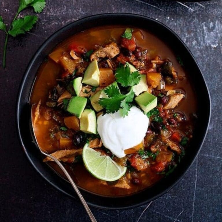 South Western Turkey Stew in a black bowl garnished with a dollop of sour cream, diced avocado, cilantro and lime wedge.