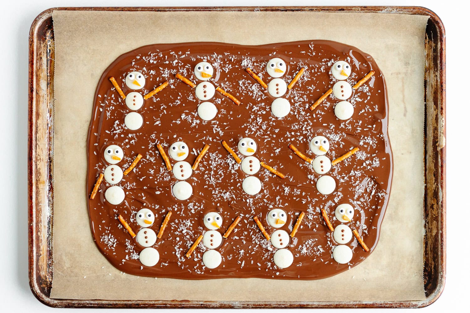 Finished snowmen assembled on chocolate bark on a parchment lined baking sheet.