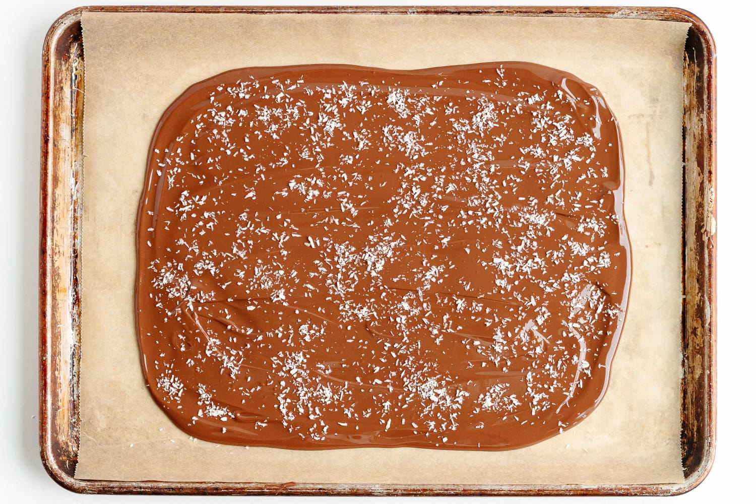 Melted chocolate sprinkled with dried coconut on a parchment lined baking sheet.