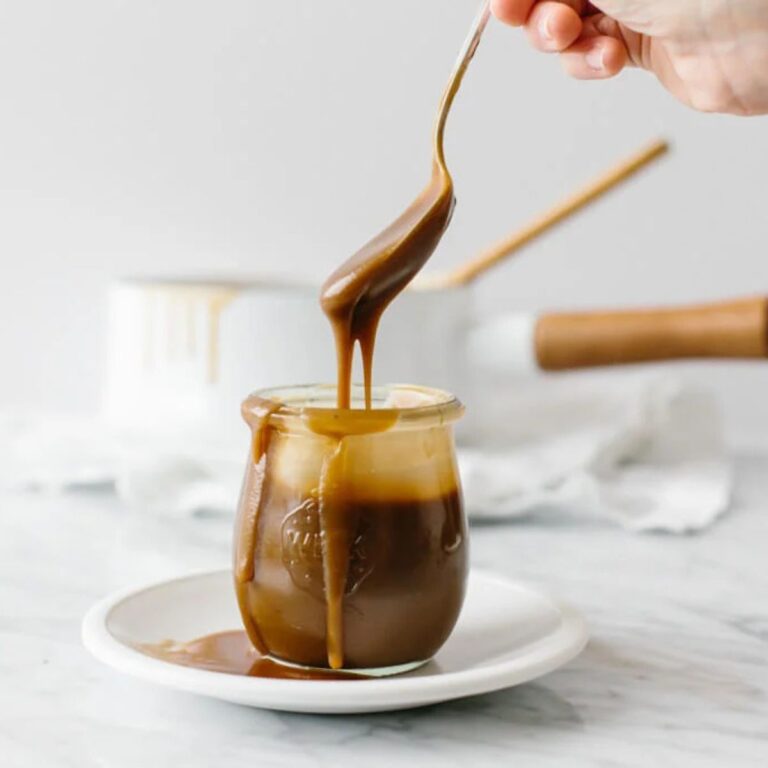 Spoonful of salted caramel being drizzled into a glass jar.