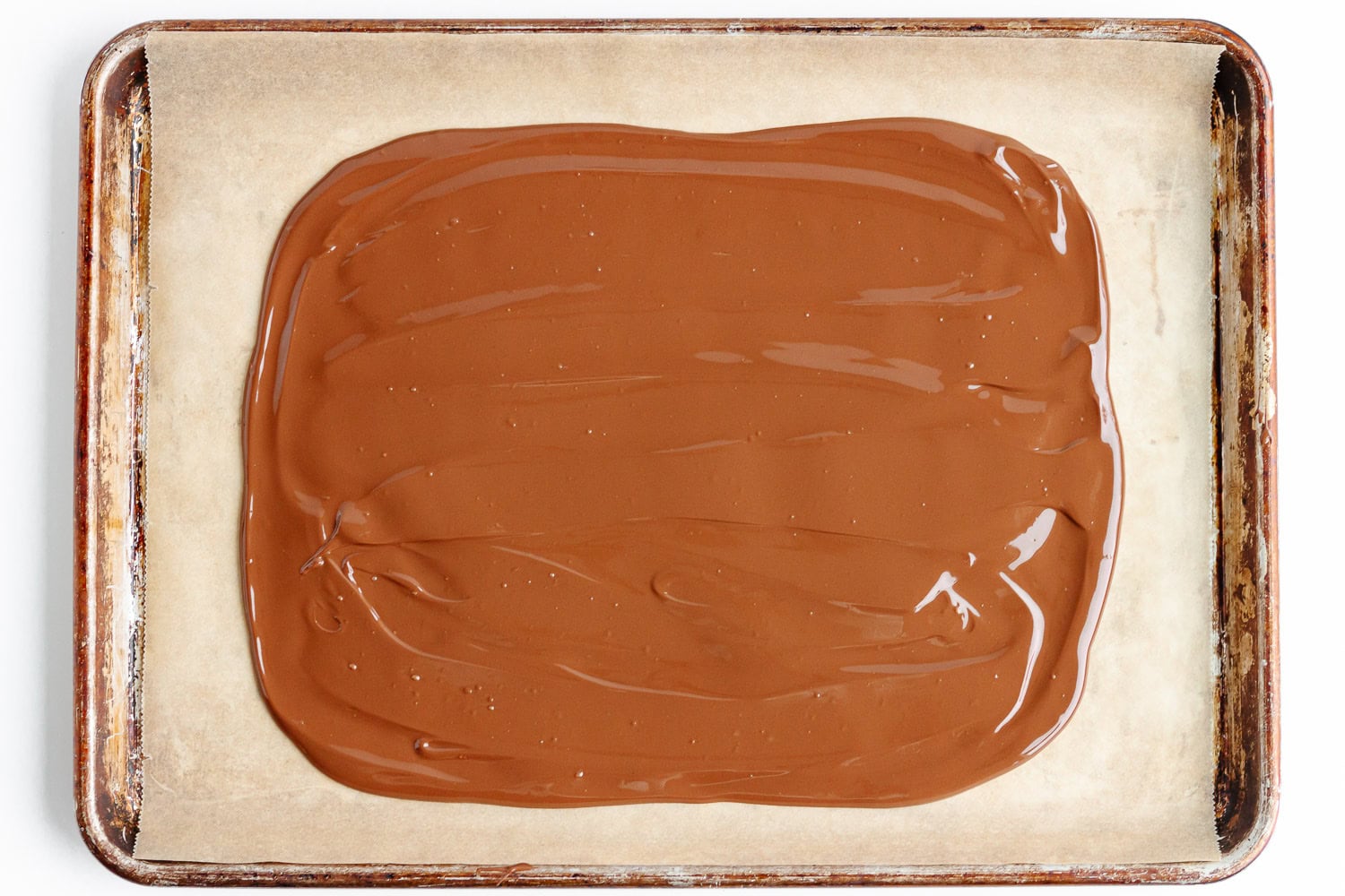 Melted chocolate spread out into rectangular shape on parchment lined baking sheet.