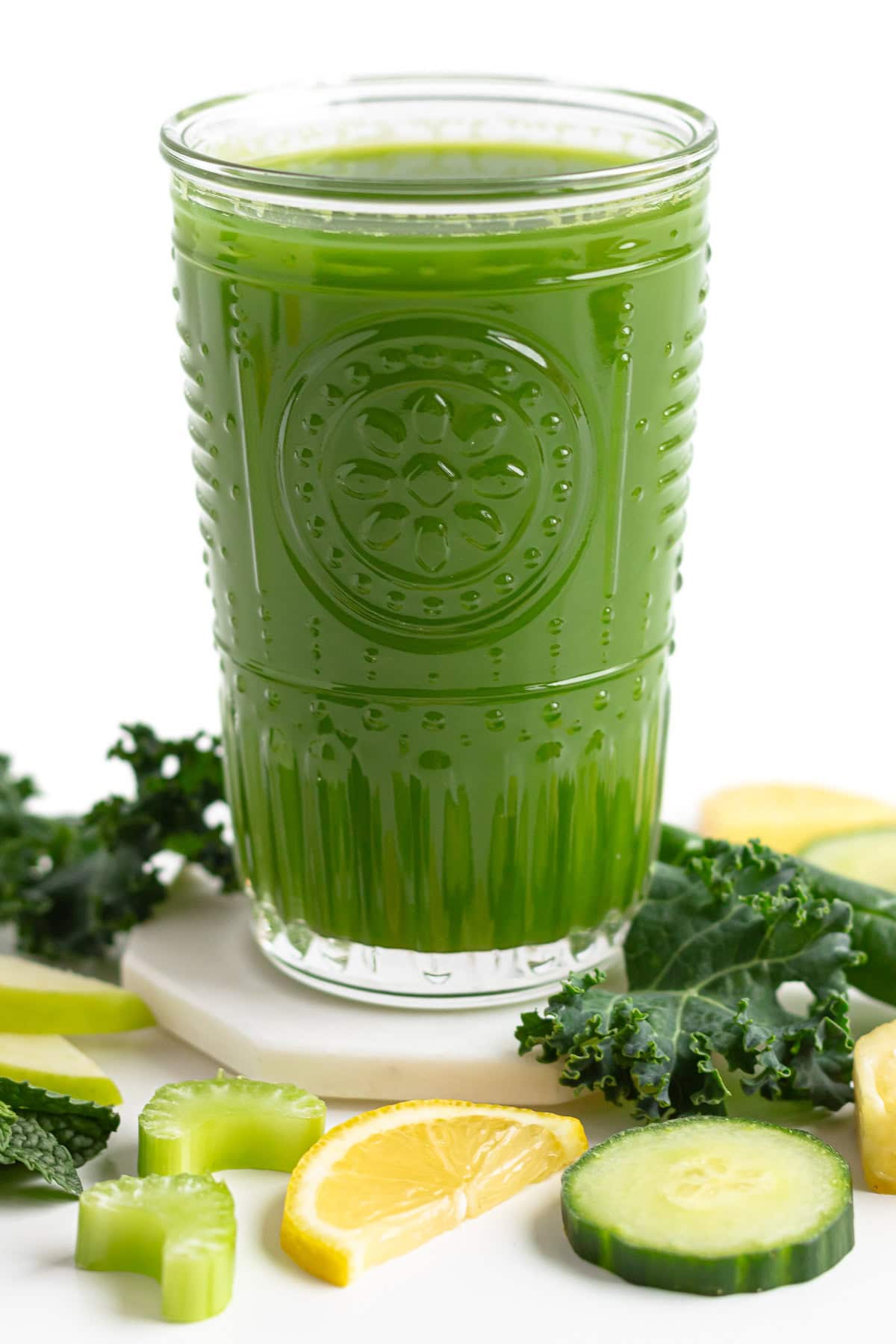 Glass of blender green juice surrounded by some of the ingredients it contains.