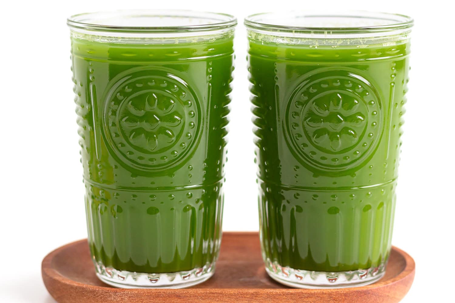 Two glasses of green juice sitting on a small wooden tray.