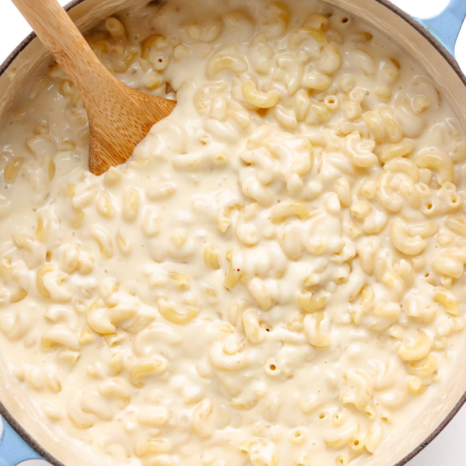 Macaroni and white cheddar sauce being stirred together with a wooden spoon.