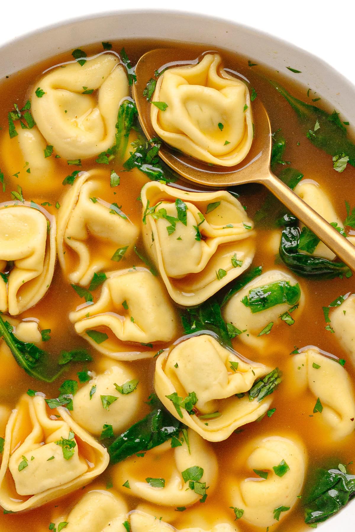 Closeup of easy tortellini soup in a white bowl with gold spoon.