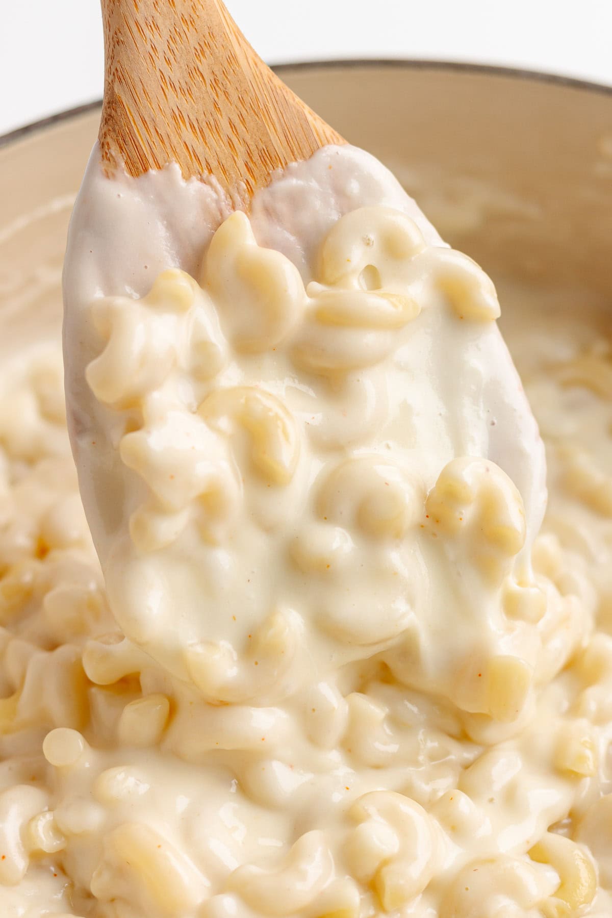 Closeup of wooden spoon stirring stovetop white cheddar mac and cheese.