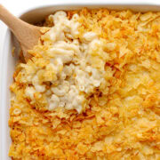 Wooden spoon lifting scoop of white cheddar mac and cheese from casserole dish.