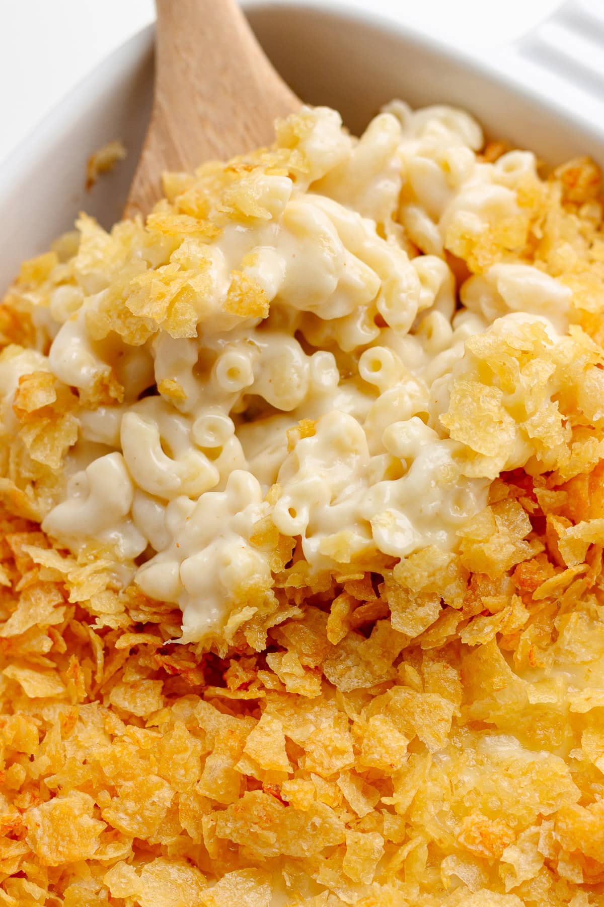 Scoop of white cheddar mac and cheese with chip topping being lifted from casserole dish.