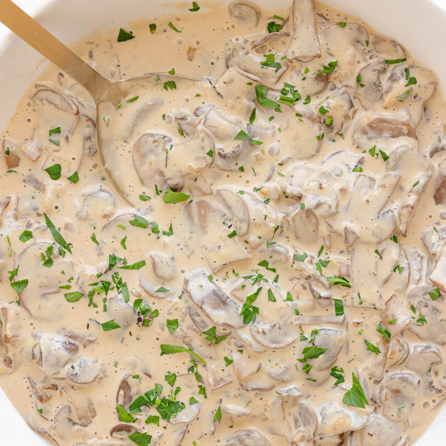 Creamy mushroom sauce in white serving bowl with a gold serving spoon.