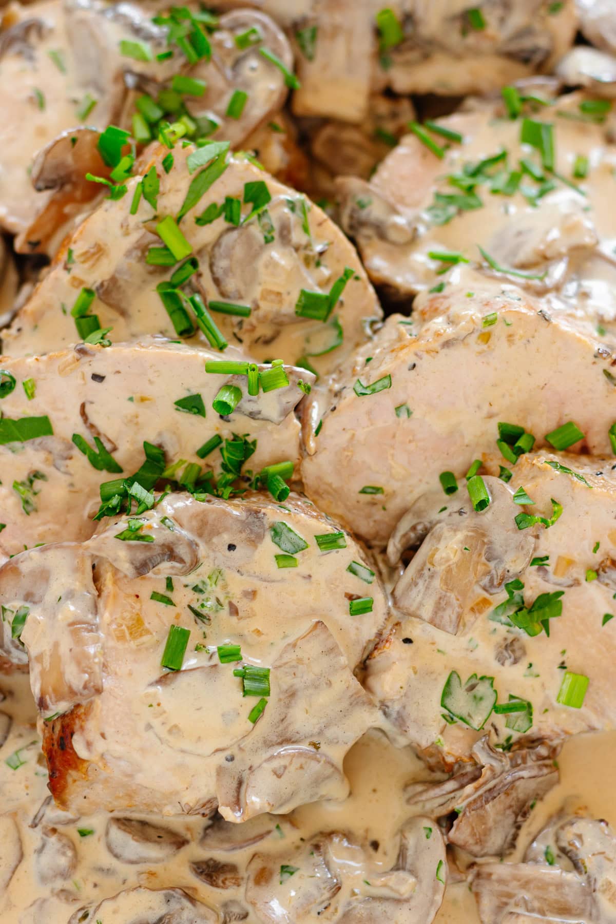 Pork tenderloin slices covered with creamy mushroom sauce and a garnish of chopped parsley and chives.