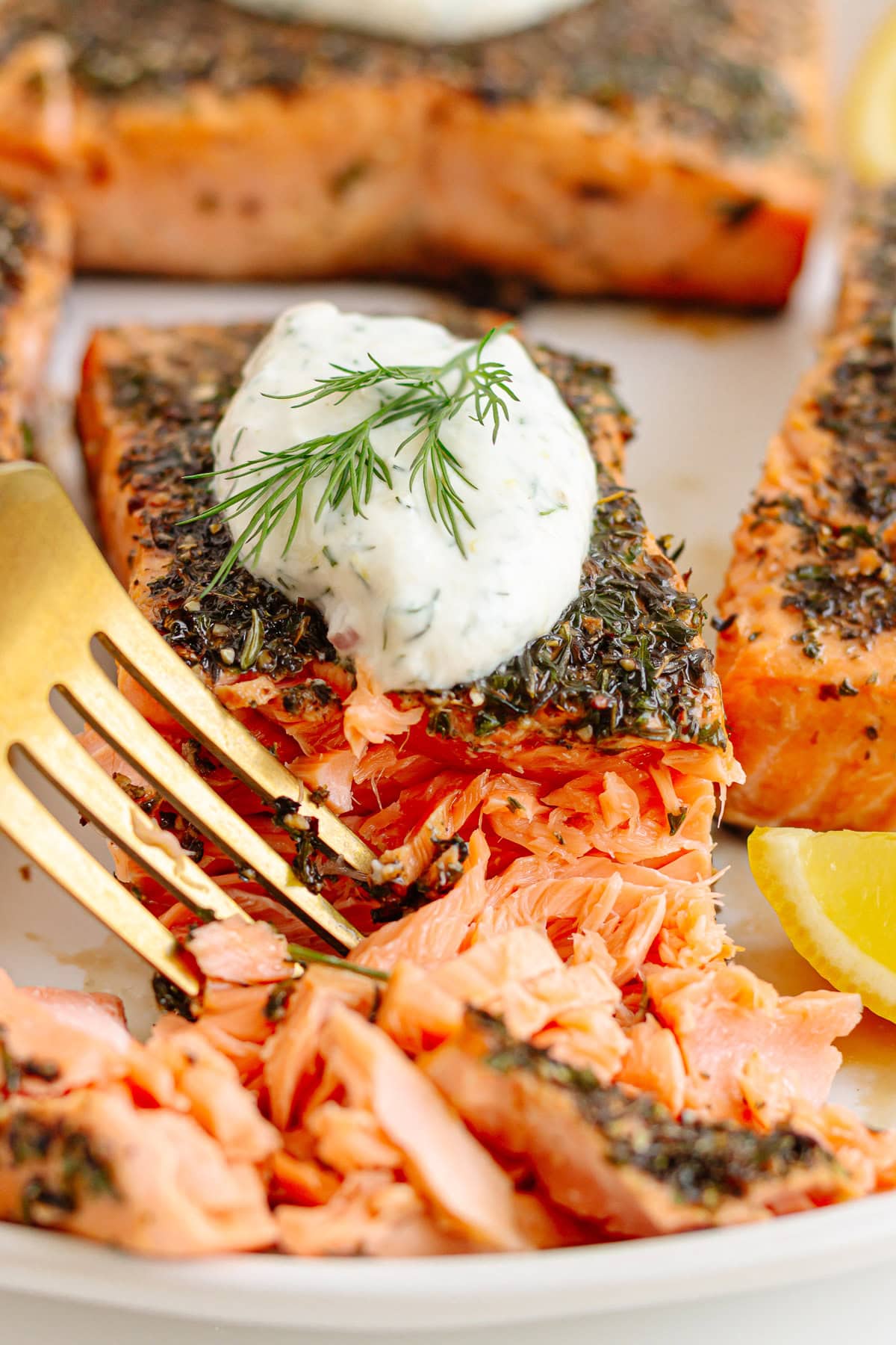 Fork flaking off pieces of a herb crusted salmon filet.