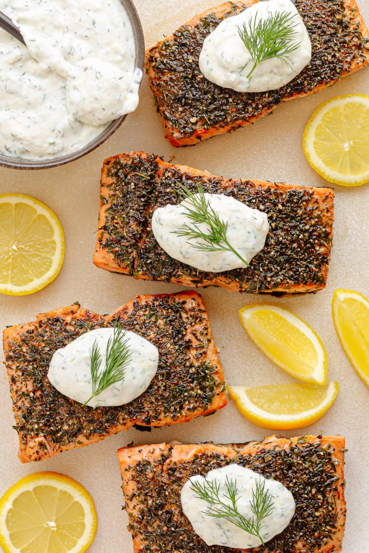 Herb crusted salmon filets on a platter with lemon dill sour cream sauce and lemons.