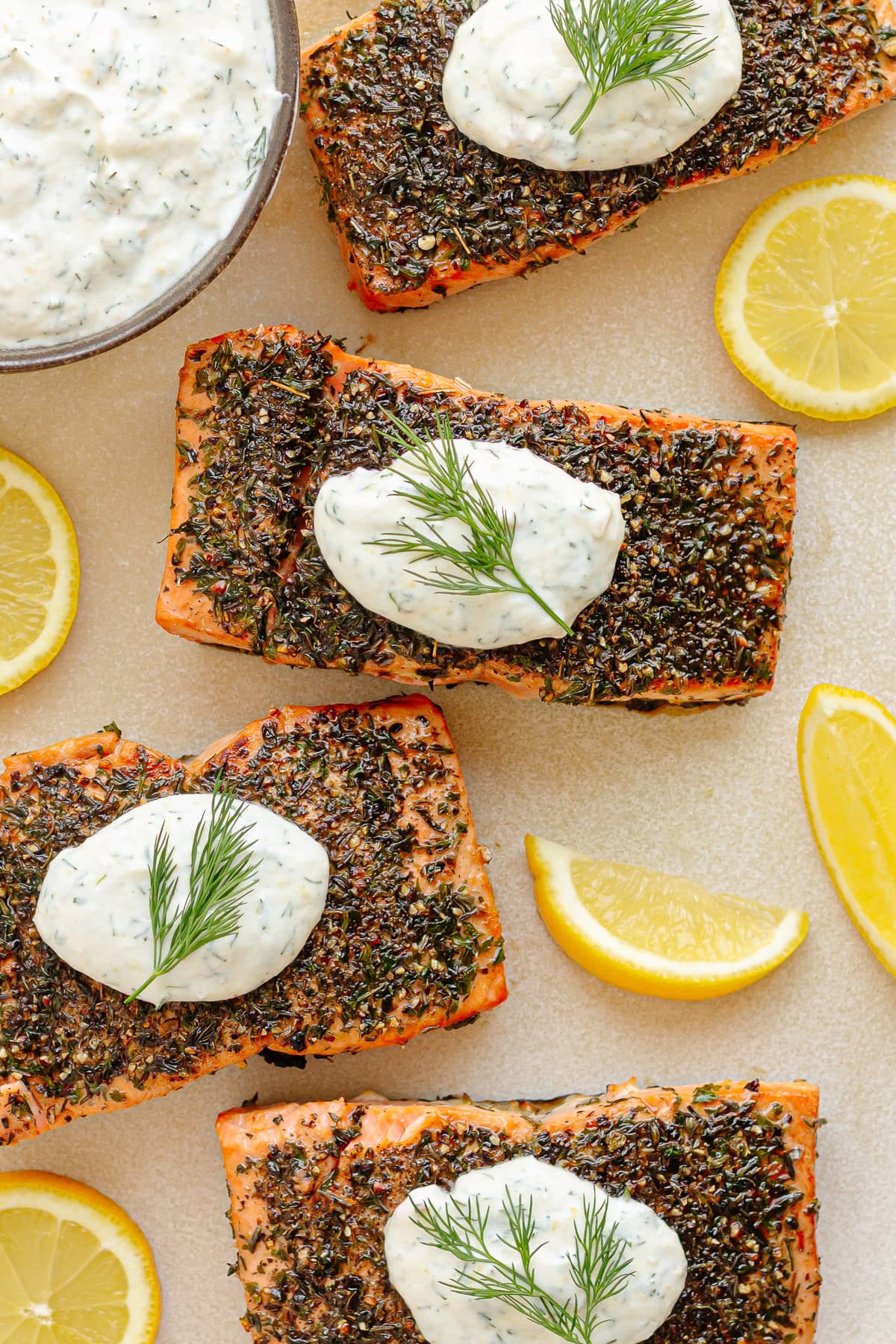 Herb crusted salmon on a platter with lemon dill sour cream sauce and lemon slices.