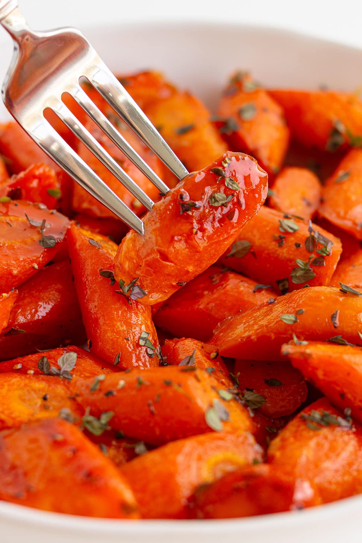 Fork picking up a honey glazed roasted carrot from serving dish.