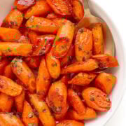 Honey thyme roasted carrots in a white serving dish with serving spoon.