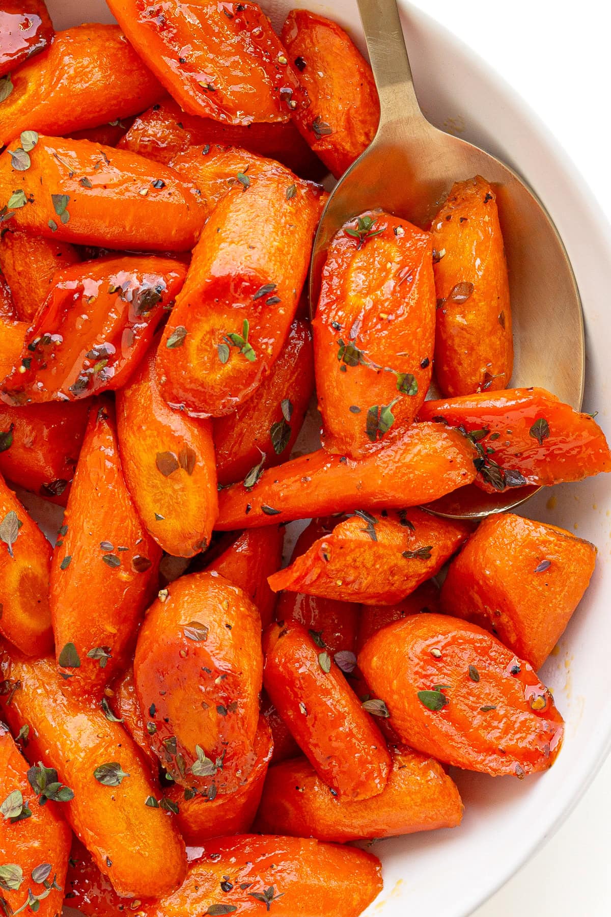 White serving dish of honey thyme roasted carrots with serving spoon.