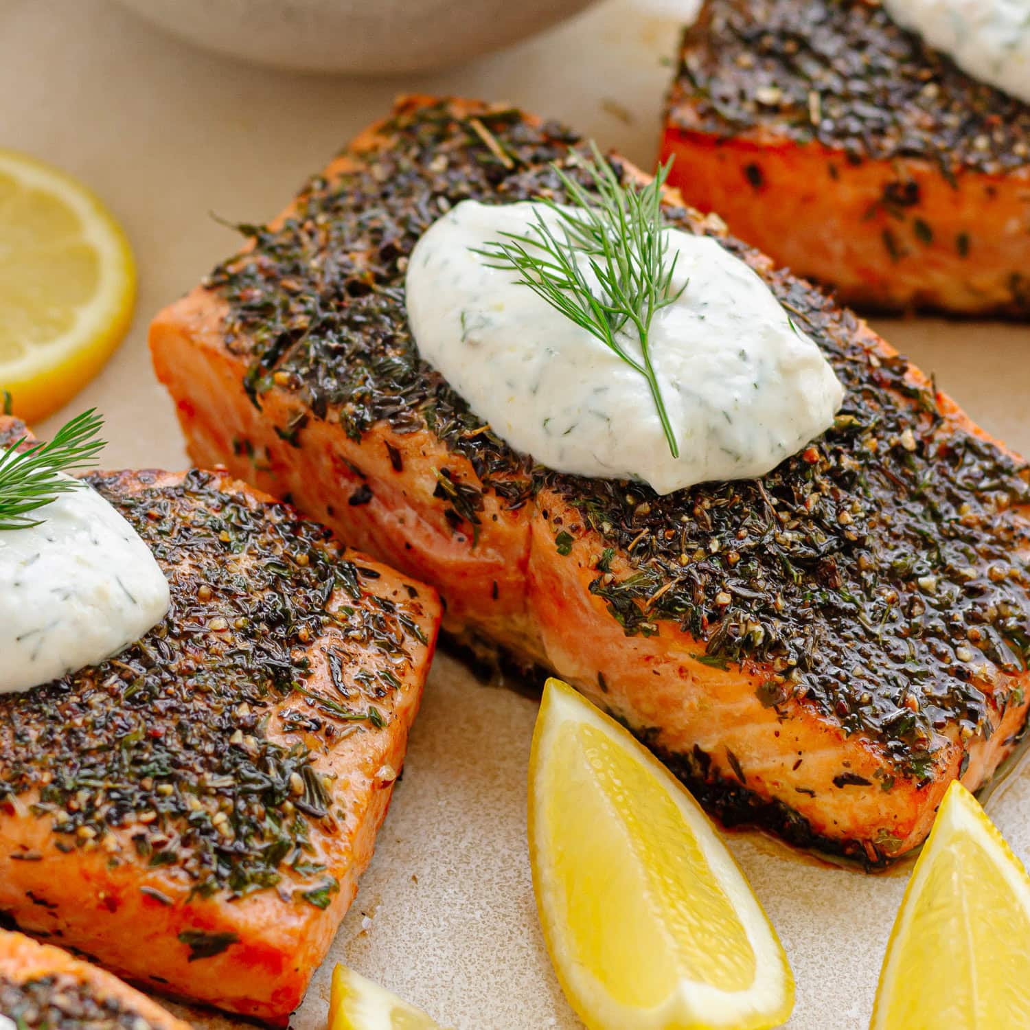 Closeup of herb crusted salmon filet topped with a dollop of lemon dill sour cream sauce and a sprig of fresh dill.