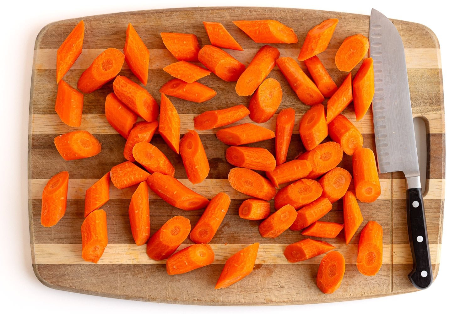 Sliced carrots for roasting on a wooden cutting board with knife.