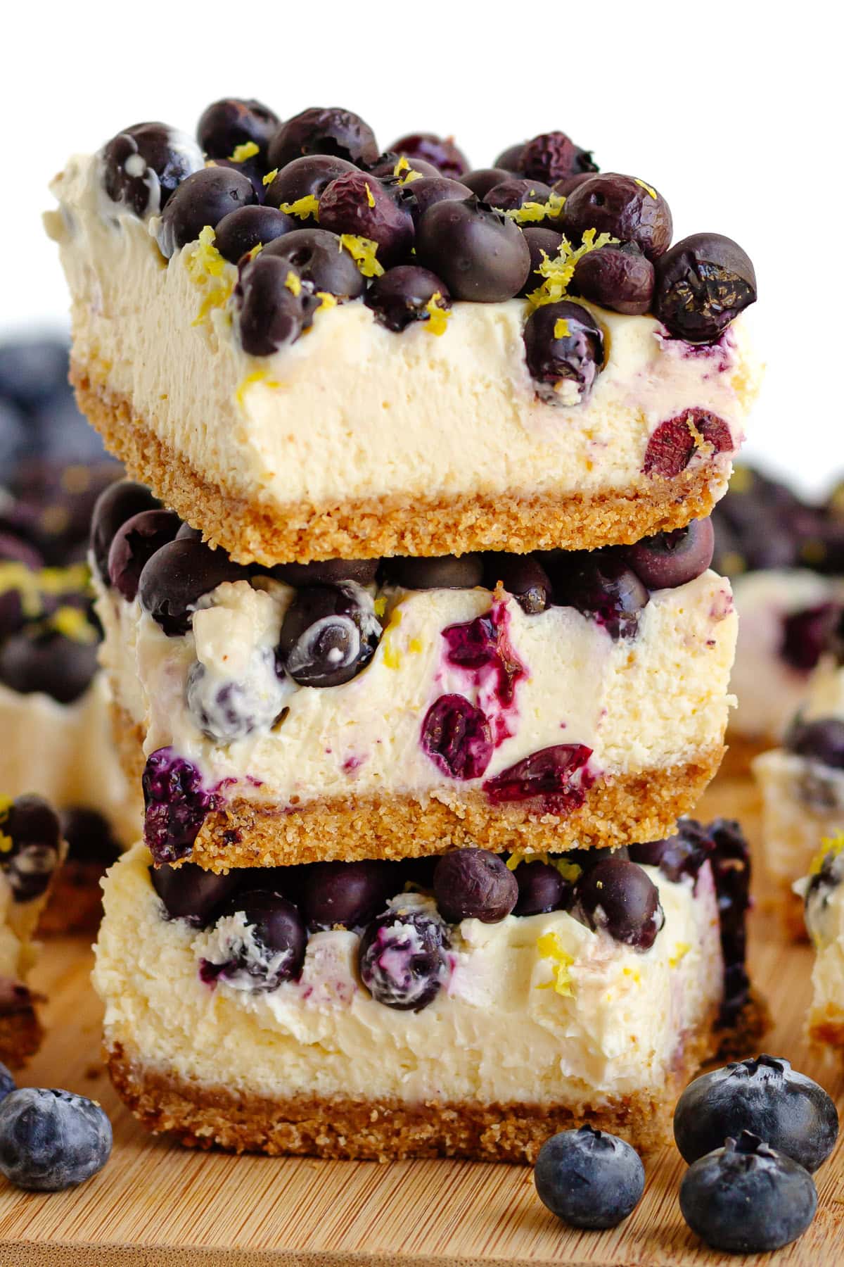 Blueberry cheesecake bars piled up on a wooden board.
