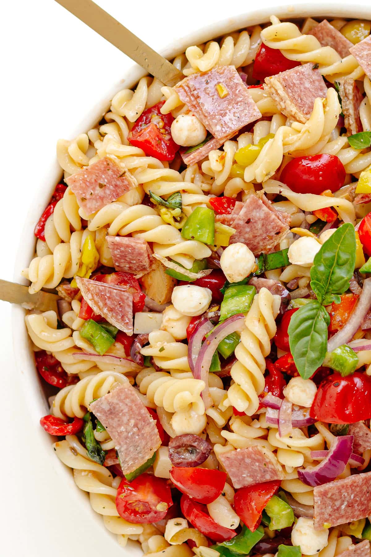 Salad servers sticking out of a bowl of antipasto pasta salad with zesty Italian dressing.