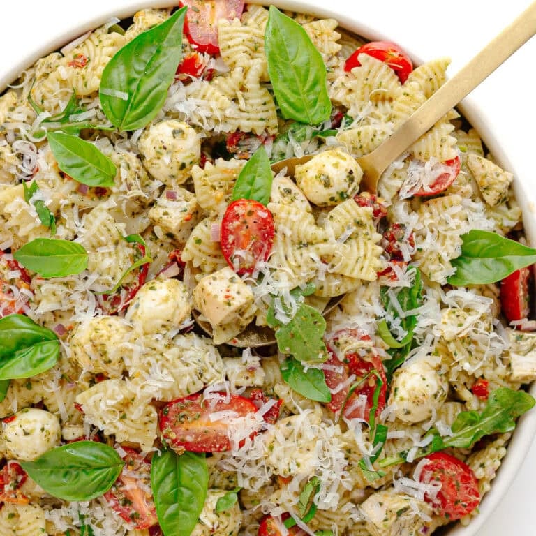 Chicken pesto pasta salad in a white serving bowl with serving spoon.