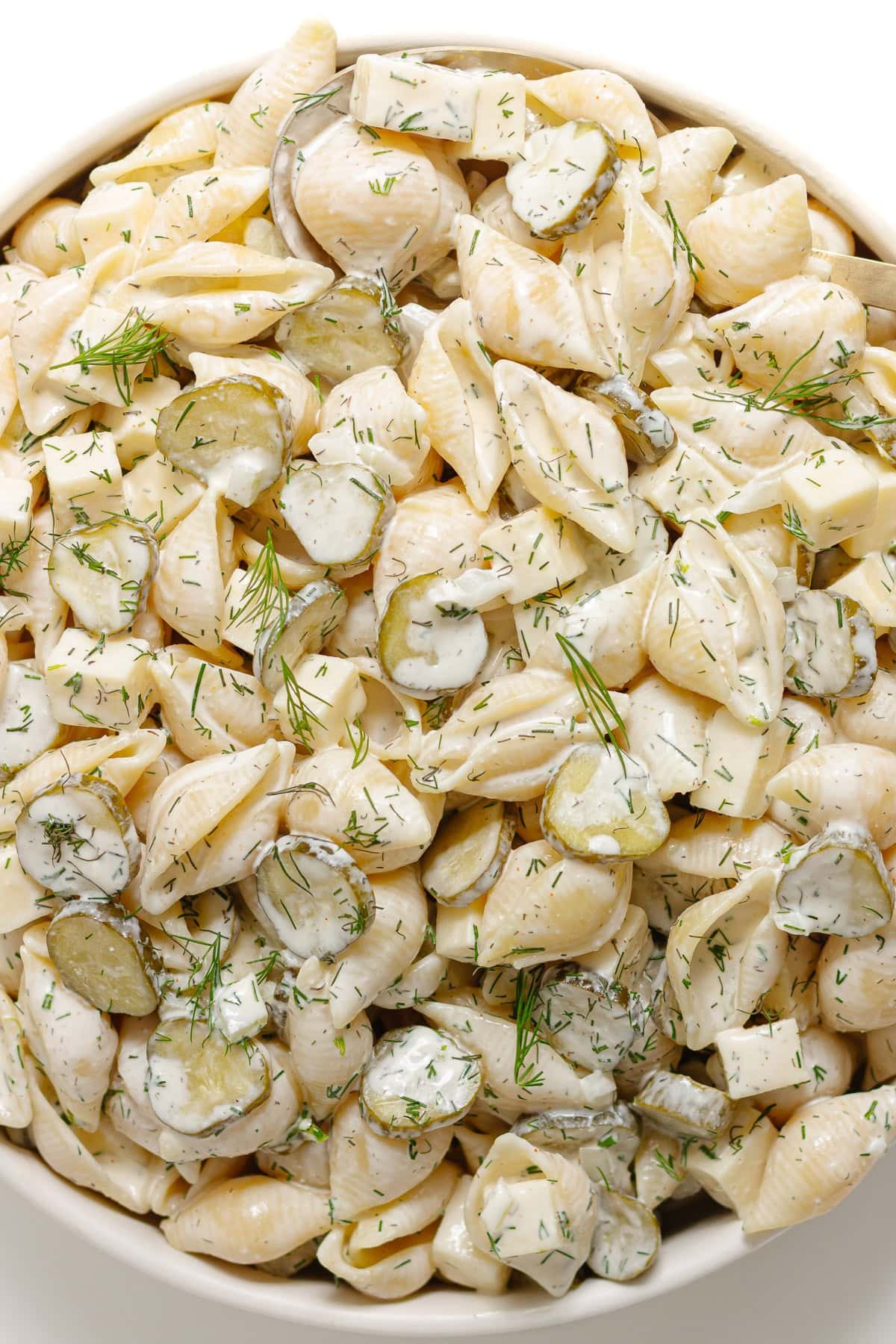 Dill pickle pasta salad in a white serving bowl with gold serving spoon.