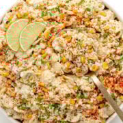 Elote pasta salad in a white serving bowl garnished with lime slices.