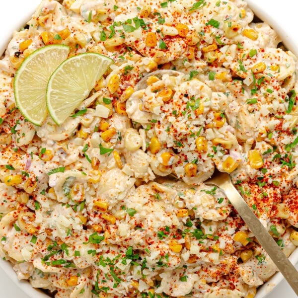 Elote pasta salad in a white serving bowl garnished with lime slices.