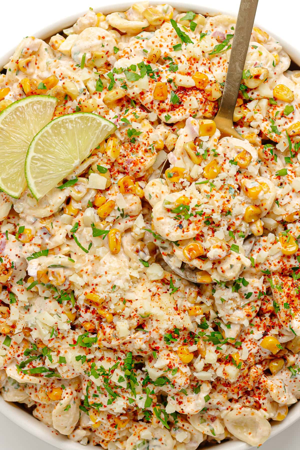 Elote pasta salad in a white serving bowl with gold colored serving spoon.