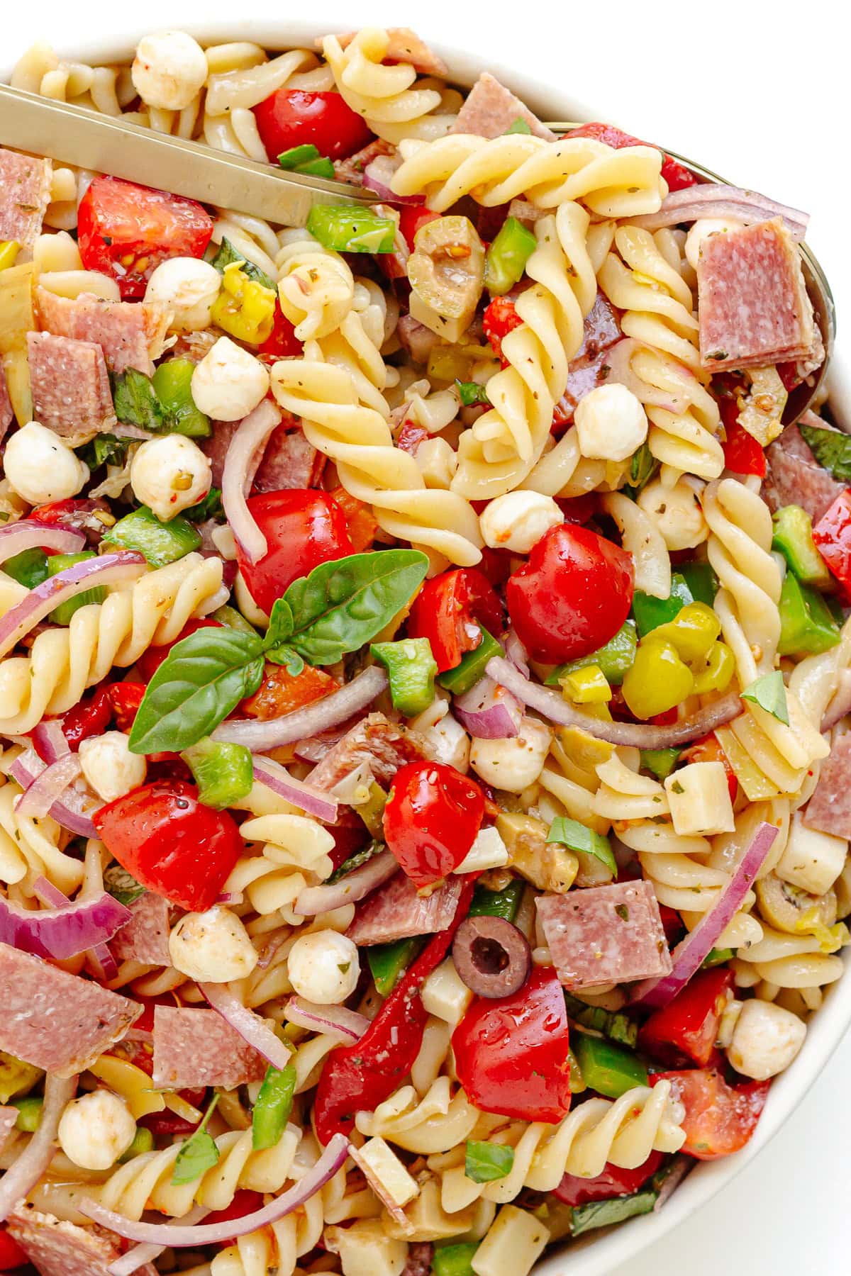 Italian pasta salad in a white serving bowl with serving spoon scooping some up.