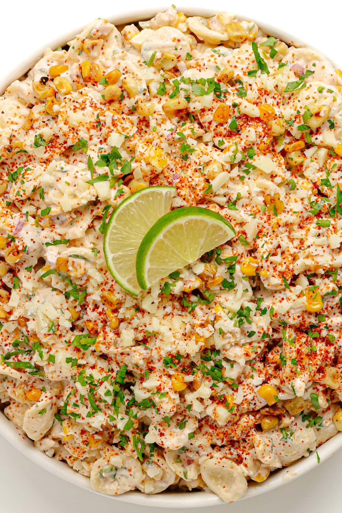 Serving bowl of Mexican street corn pasta salad garnished with lime slices.