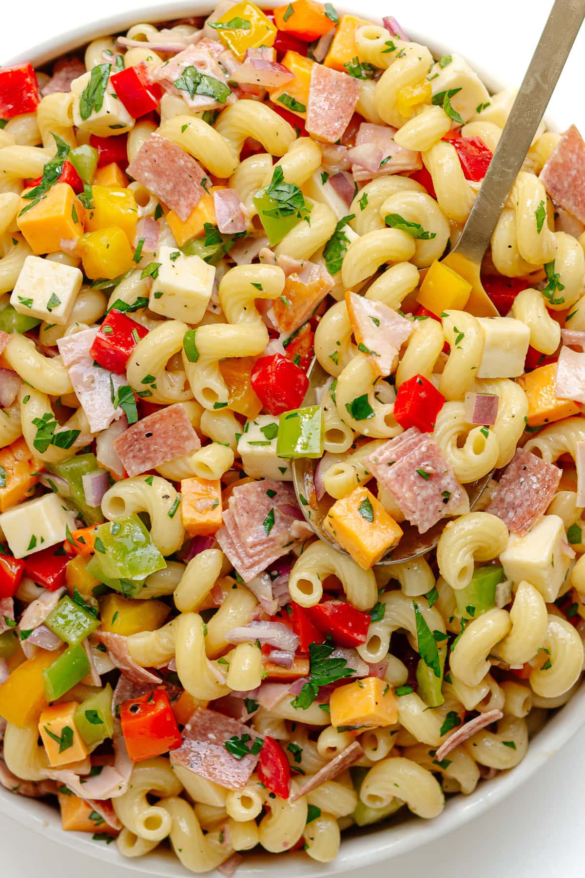 My go-to pasta salad in a white serving bowl with gold colored serving spoon.
