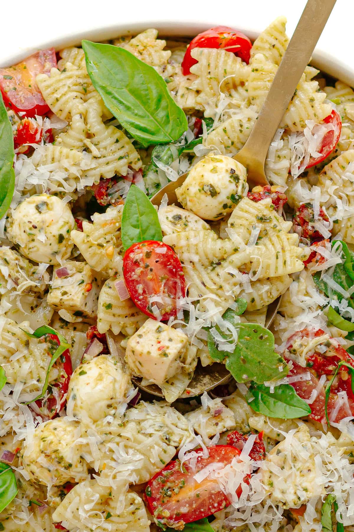 Closeup of serving spoon scooping up some pesto pasta salad with chicken.