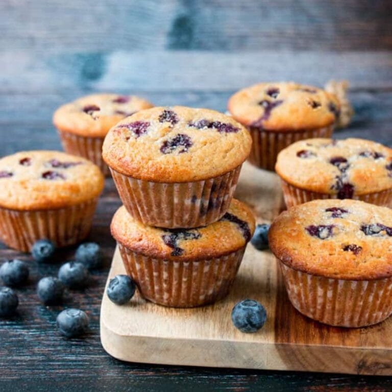 Blueberry muffins stacked on a wooden cutting board.