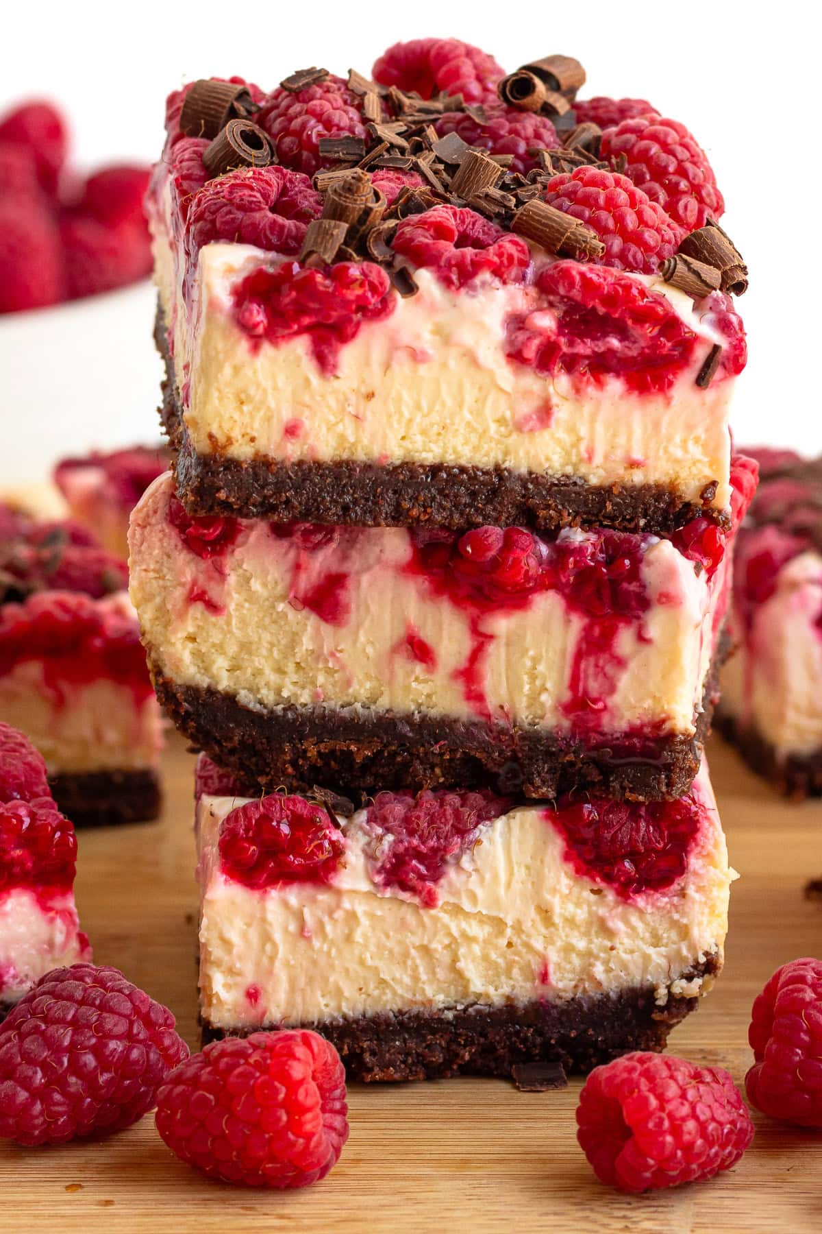 Stack of raspberry cheesecake bars with chocolate graham cracker crust and dark chocolate shavings on top.