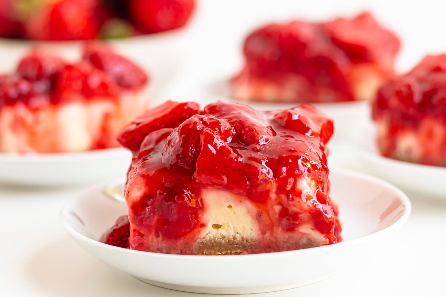 Strawberry cheesecake bars on small white serving plates.