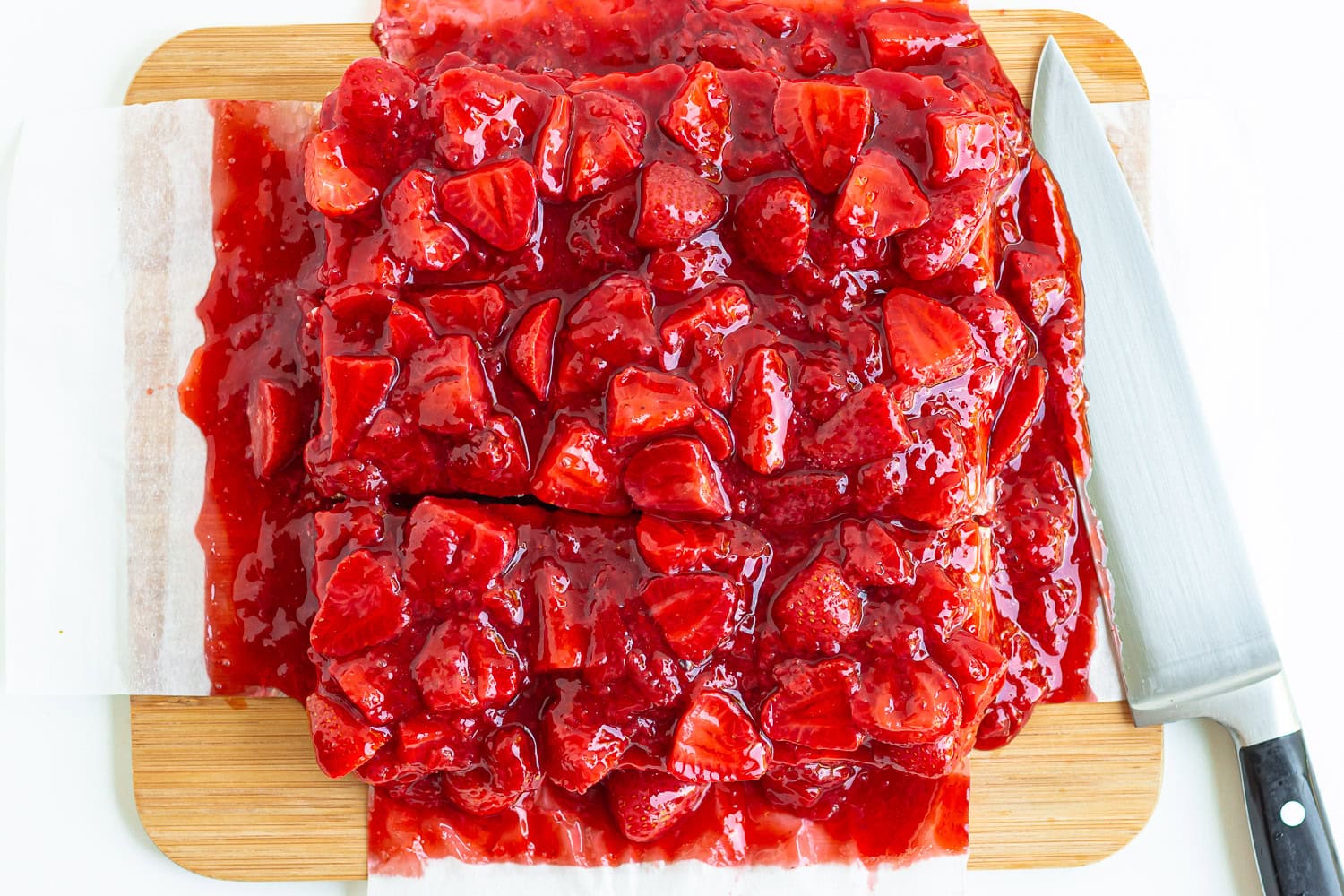 Slicing strawberry cheesecake bars on a wooden cutting board.